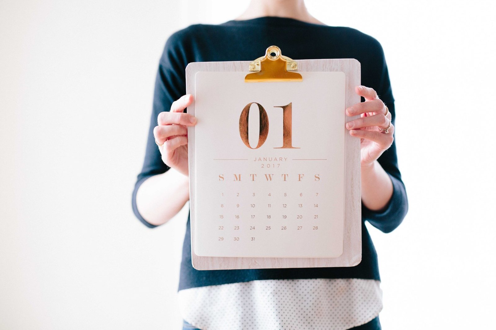Person holding a clipboard calendar showing the first of the month