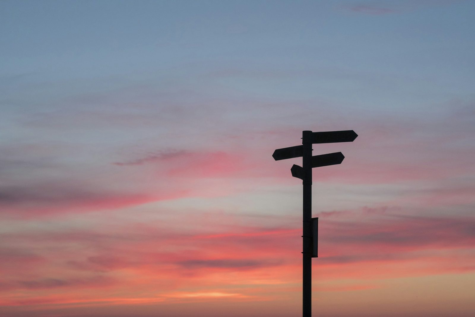 Signpost silhouetted against a pink sunset sky
