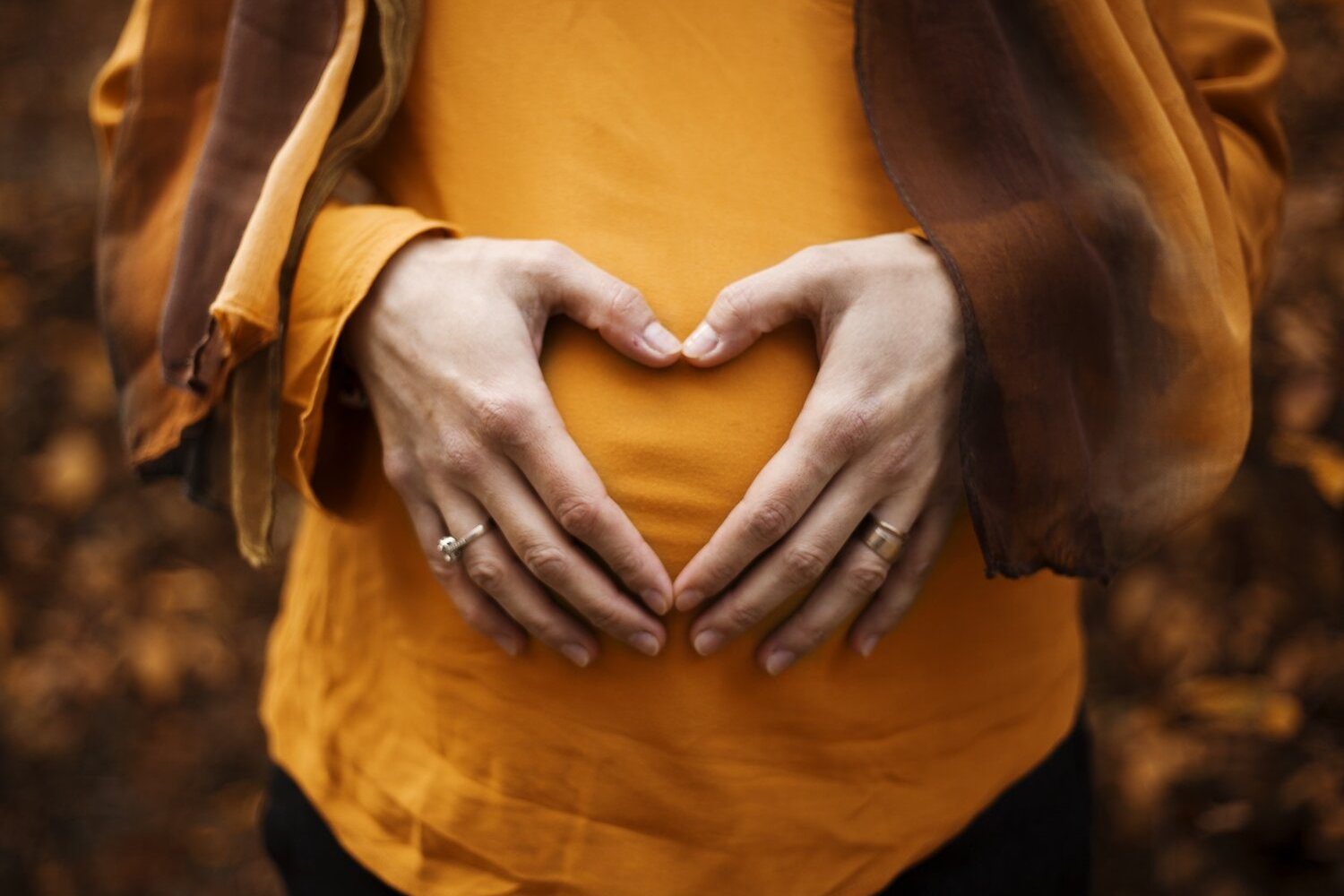 Hands forming a heart shape over a pregnant bump