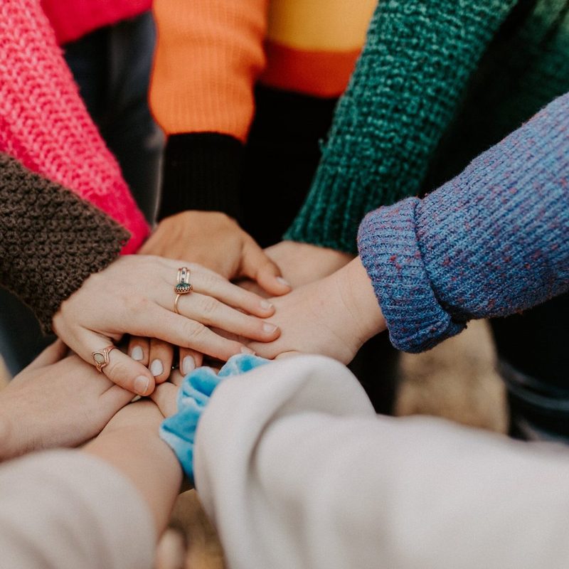 Group of hands in colourful knitted sleeves stacked together in support