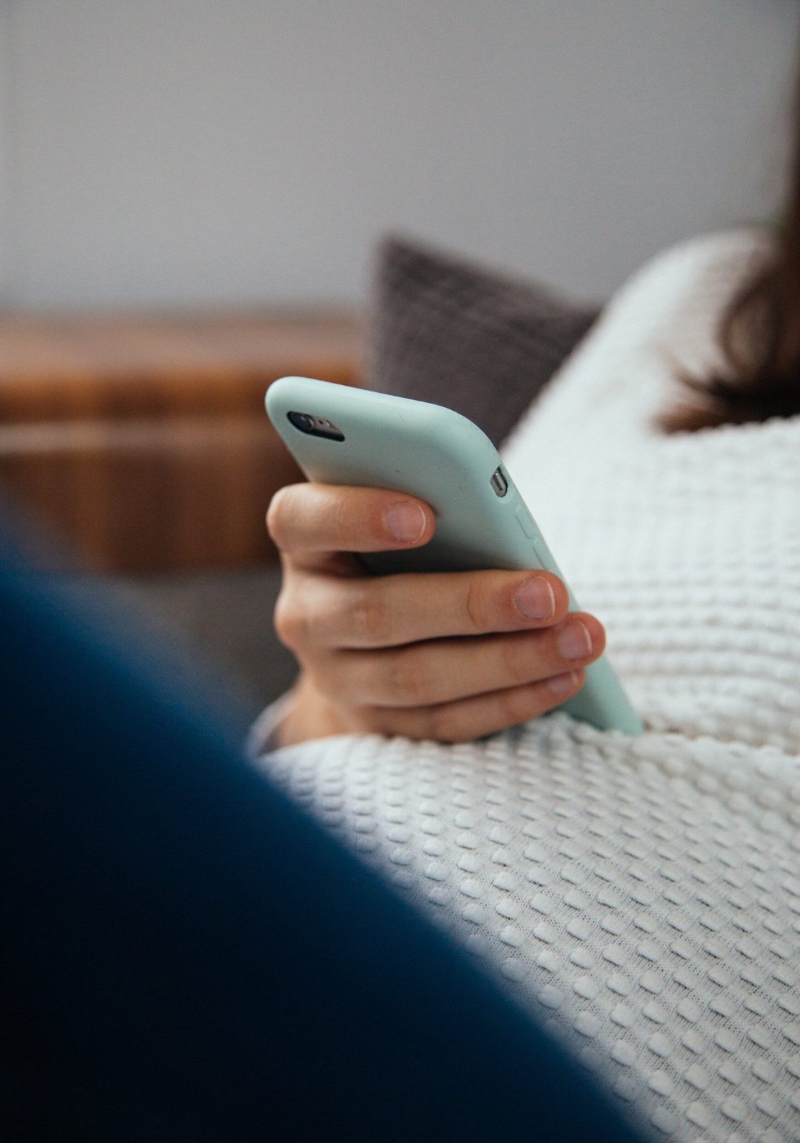 Hand holding a mobile phone on a cosy knitted blanket