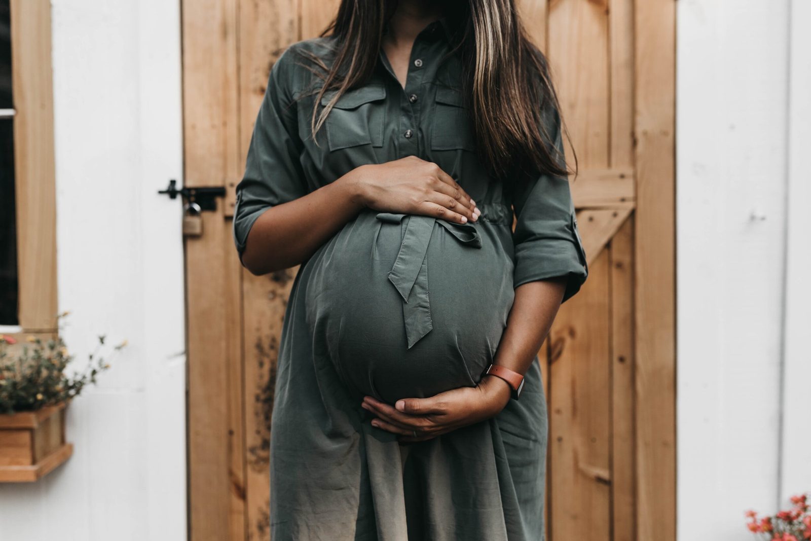 Pregnant woman in a green dress cradling her bump beside a wooden door