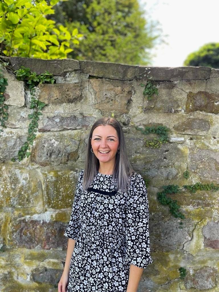 Lea White, hypnobirthing teacher, smiling in front of an old stone wall