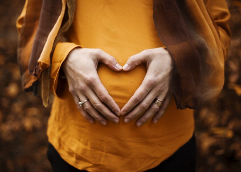 Hands forming a heart shape over a pregnant bump