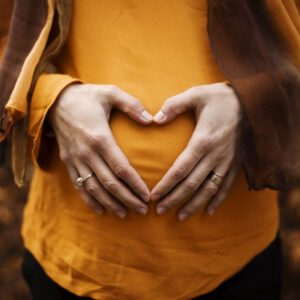 Hands forming a heart shape over a pregnant bump